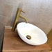 Brushed brass basin mixer tap with curved spout beside a white oval vessel sink