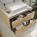 Bathroom vanity with open drawer displaying toiletries, set against a tiled wall.